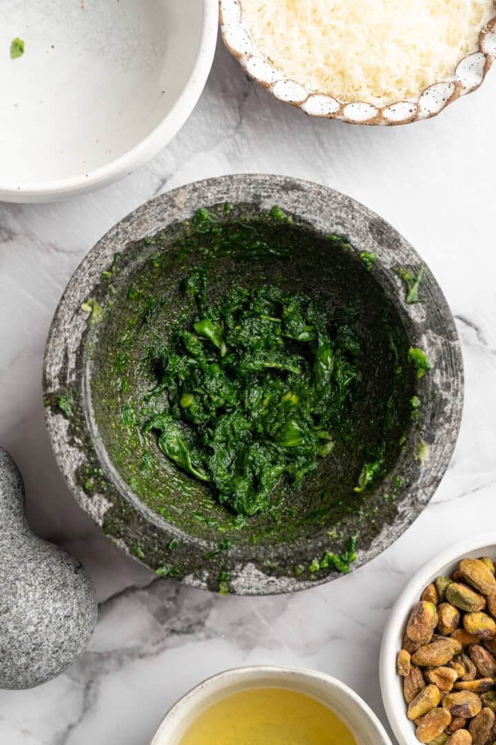 Pistachio pesto combines fresh basil leaves with nutty pistachios for a different spin on pesto. It's easy to make and so delicious! Basil mashed into pesto mixture in mortar