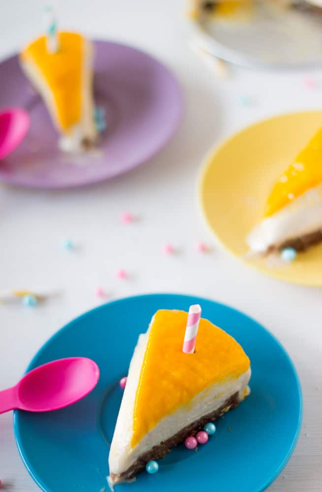 Slice Vegan Mango Coconut Cheesecake with a pink spoon on a blue plate.