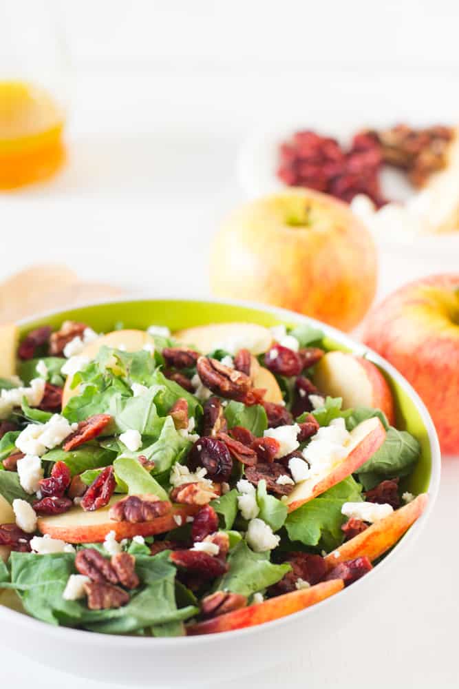 Side shot of apple pecan and feta salad with apples in the background. 