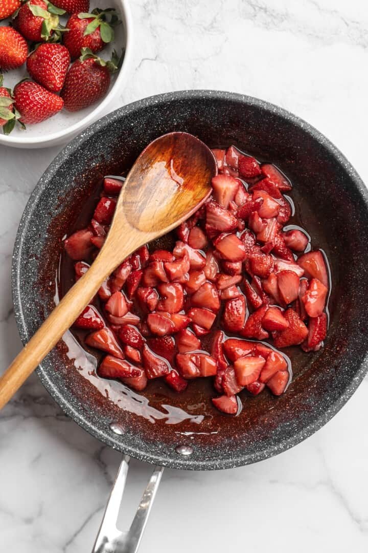Overhead view of strawberry compote in skillet with wooden spoon
