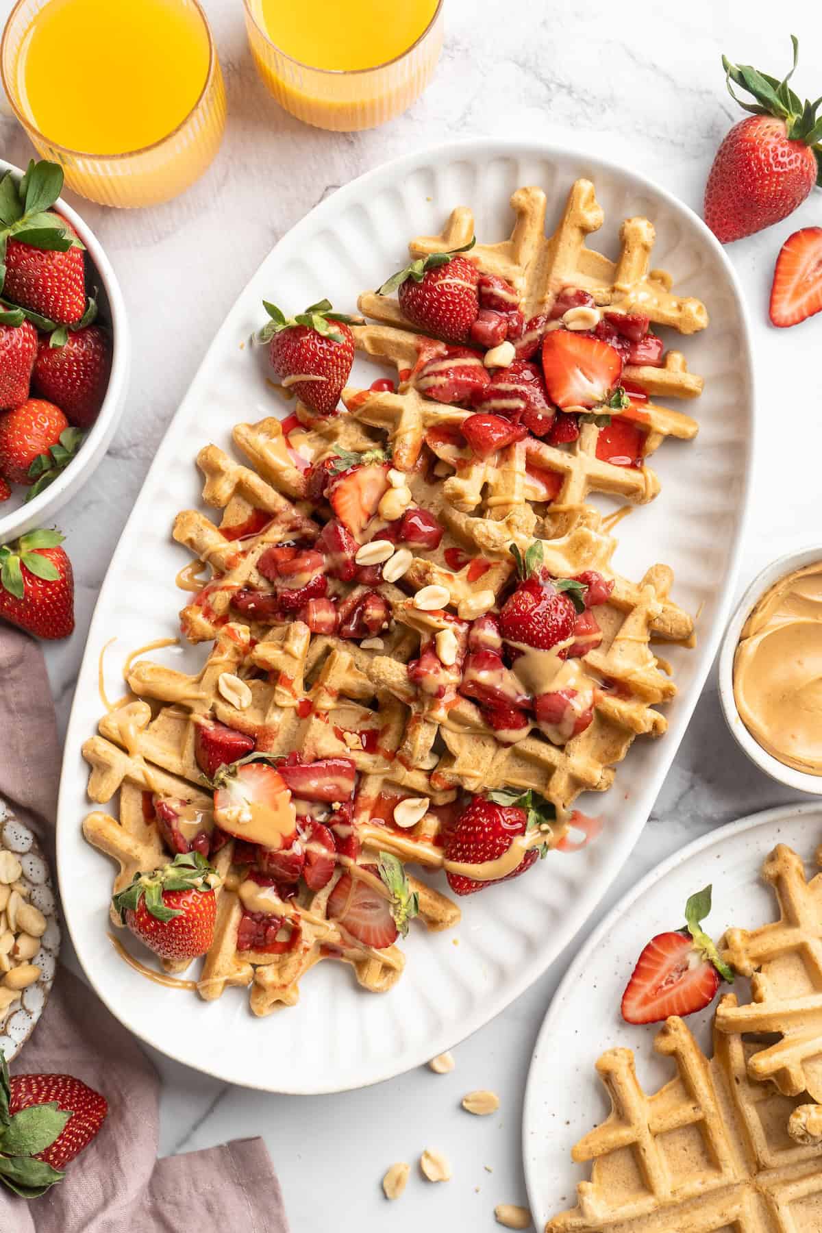 Overhead view of peanut butter waffles on platter with strawberries and compote