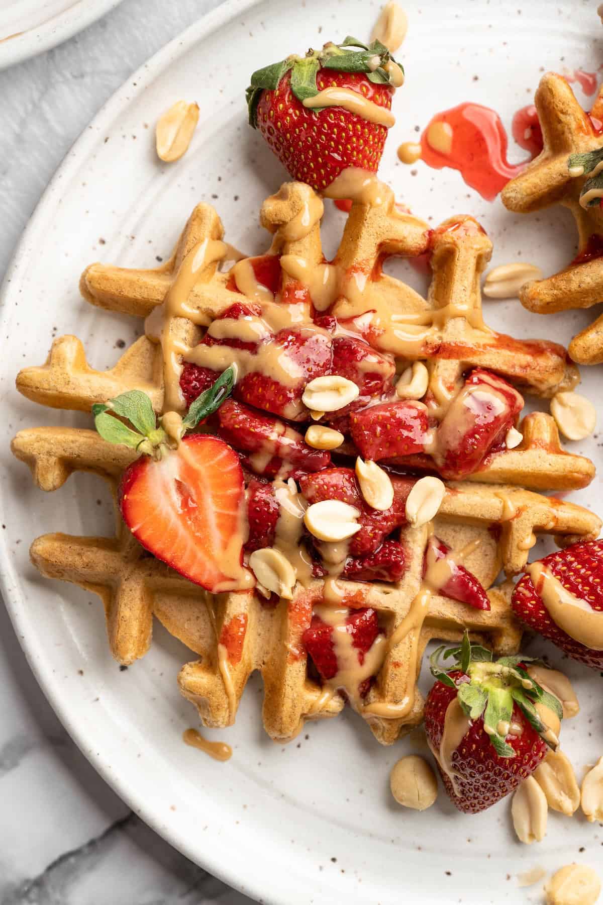 Overhead view of peanut butter and jelly waffles on plate with fresh strawberries