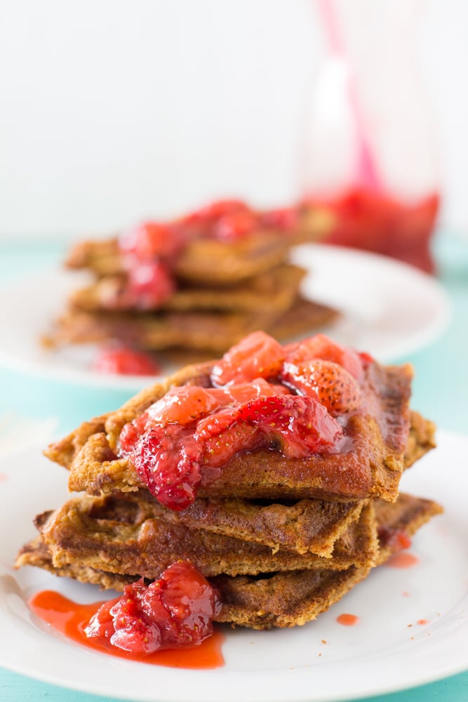 A stack of peanut butter waffles, covered in strawberry compote. 