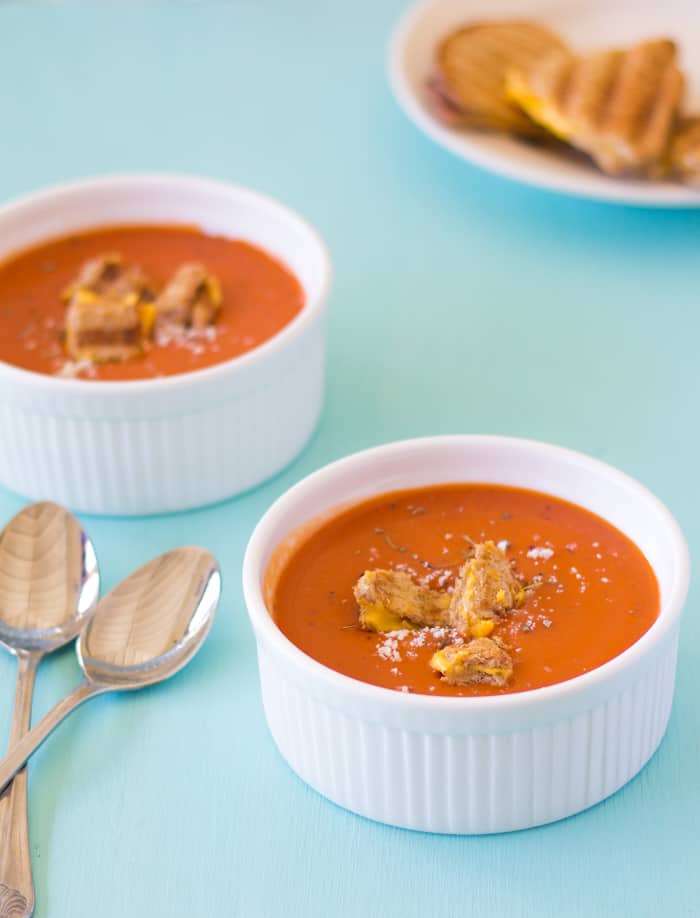 Roasted tomato soup in two ramekins with spoons on the side. 