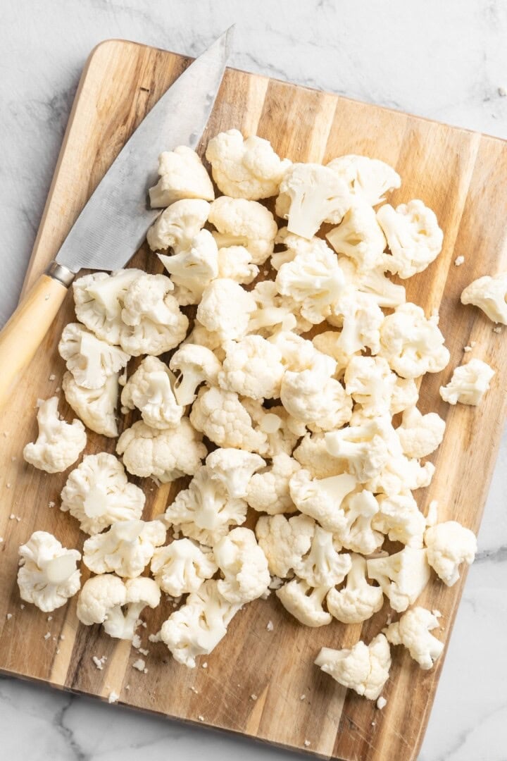 These Cauliflower Bites are crispy, crunchy and full of big flavour thanks to an irresistible sweet sriracha sauce. A total crowd pleaser! Overhead view of cauliflower cut into florets on cutting board with knife