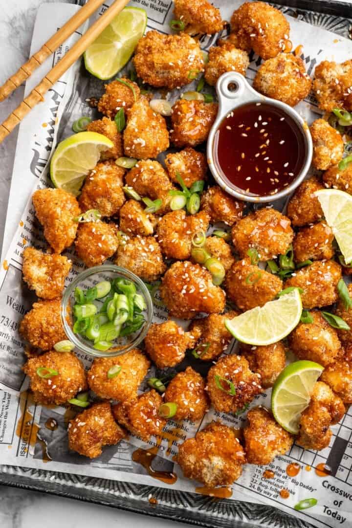 These Cauliflower Bites are crispy, crunchy and full of big flavour thanks to an irresistible sweet sriracha sauce. A total crowd pleaser! Overhead view of sweet sriracha cauliflower bites on pan with bowl of sauce and bowl of green onions