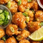Overhead view of crispy cauliflower bites with sweet sriracha sauce, lime wedge, green onions, and sesame seeds