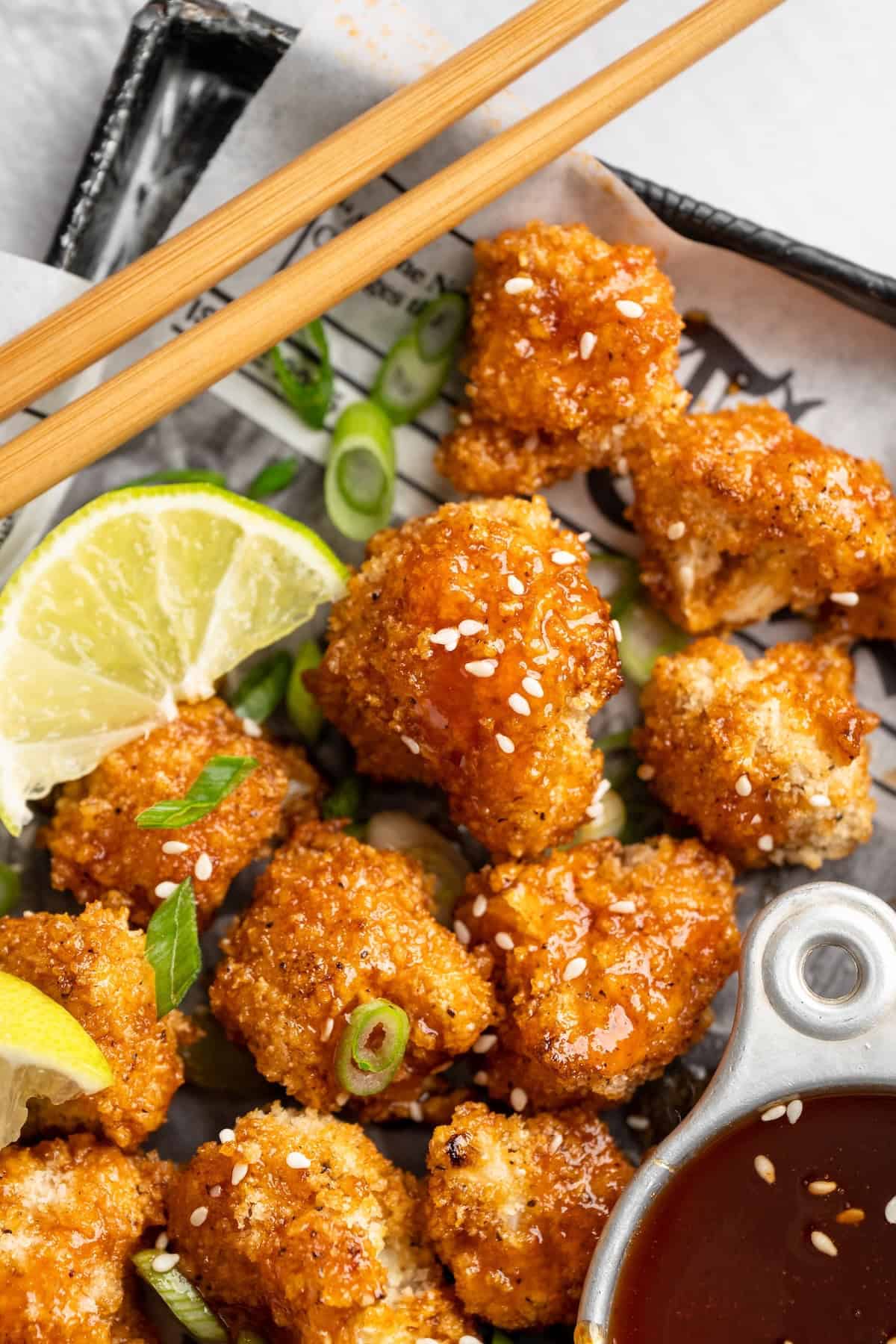 These Cauliflower Bites are crispy, crunchy and full of big flavour thanks to an irresistible sweet sriracha sauce. A total crowd pleaser! Pan of crispy cauliflower bites with bowl of sweet sriracha sauce, chopsticks, and lime wedge