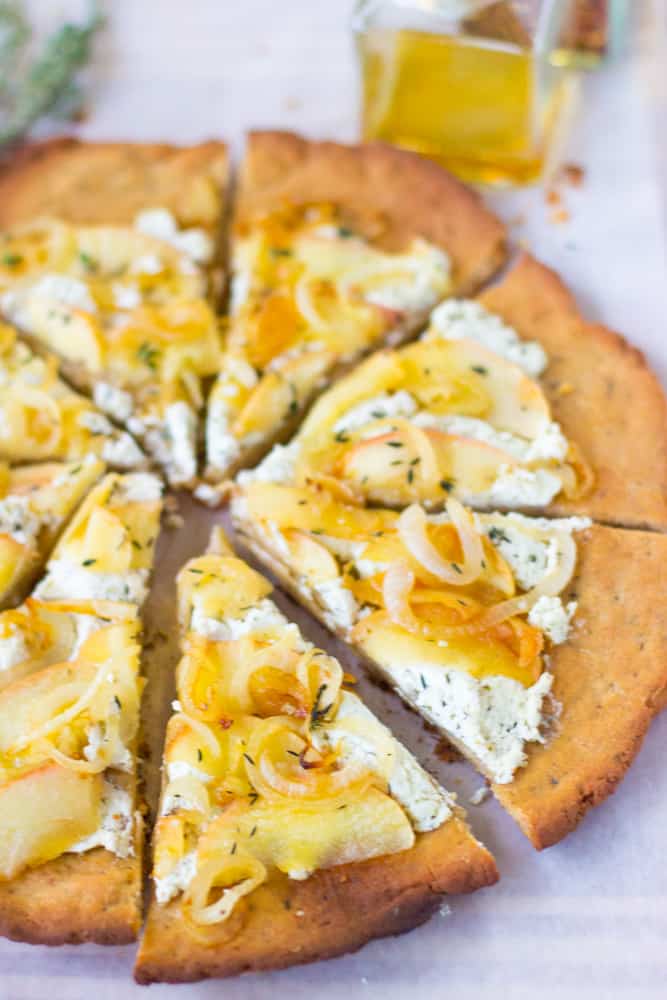 Slices of goat cheese pizza with caramelized onions and apples on a white table.  