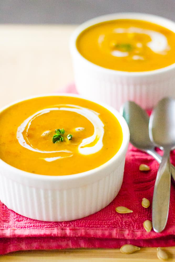 Two white bowls of pumpkin soup on a red cloth. 