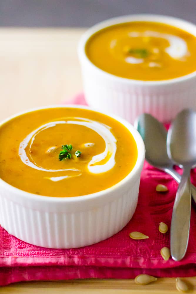 Vegan creamy pumpkin soup in two white ramekins with two spoons on the side. 