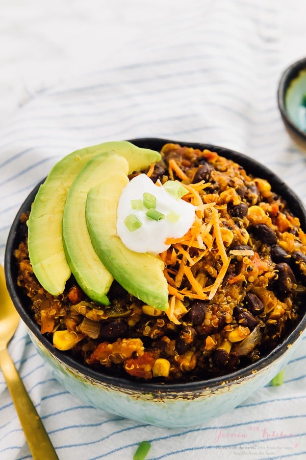 Vegan chili in a blue bowl with sour cream and slices of avocado on top. 