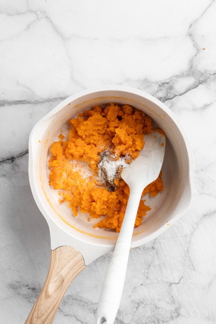 Stirring salt, pepper, milk, and mashed sweet potatoes in pan