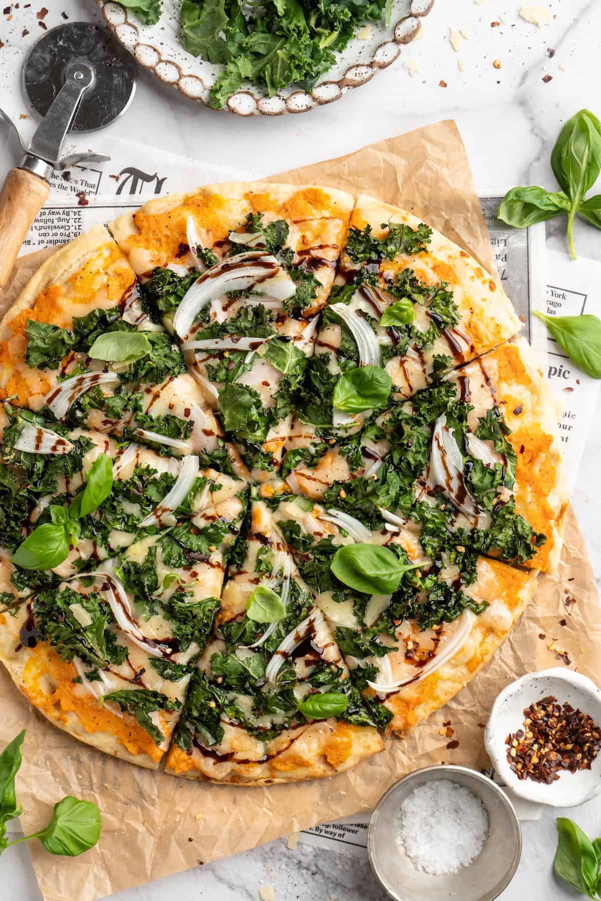 Overhead view of sliced sweet potato and kale pizza with balsamic glaze