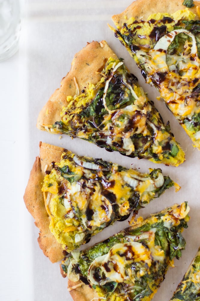 Top down shot of sweet potato and kale pizza on a white table.