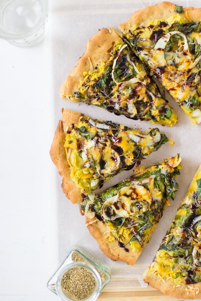 Top down shot of sweet potato and crispy kale pizza with balsamic drizzle  on a wooden board. 