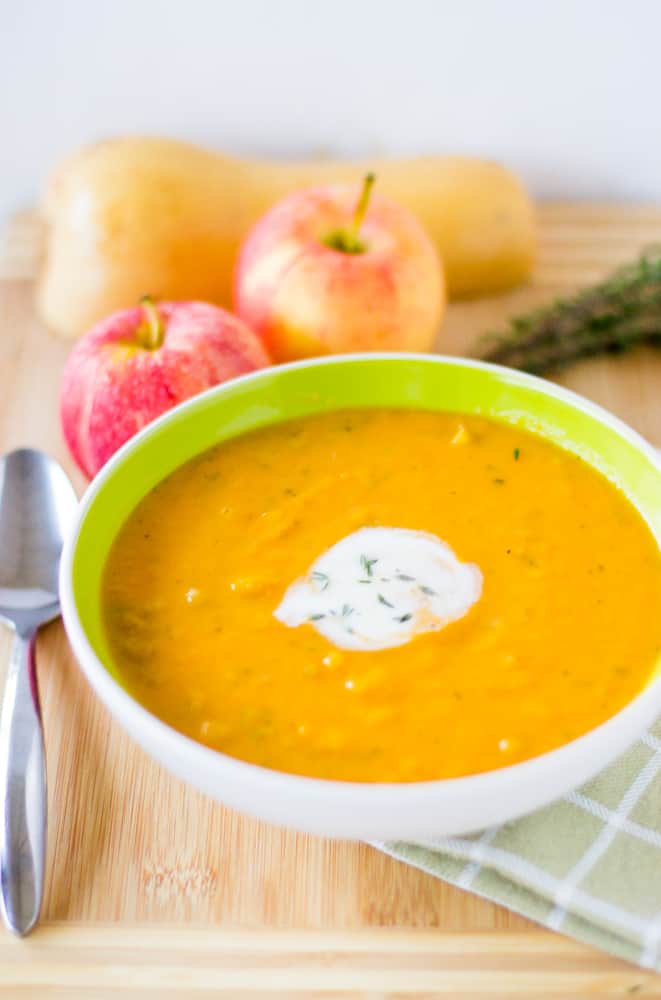 Vegan butternut squash and apple soup in a green and white bowl with cream on top. 