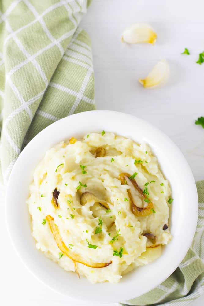 Overhead shot of vegan garlic mashed potatoes with caramelised onions in a white bowl. 