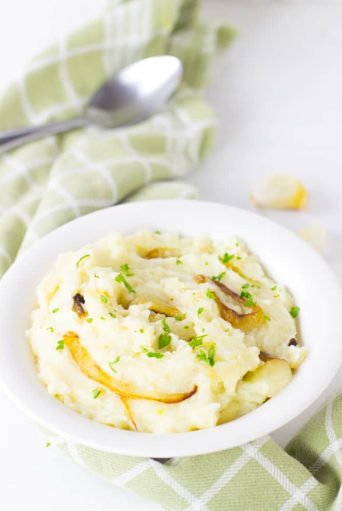 Best garlic mashed potatoes with caramelised onions in a white bowl with a spoon on the side. 