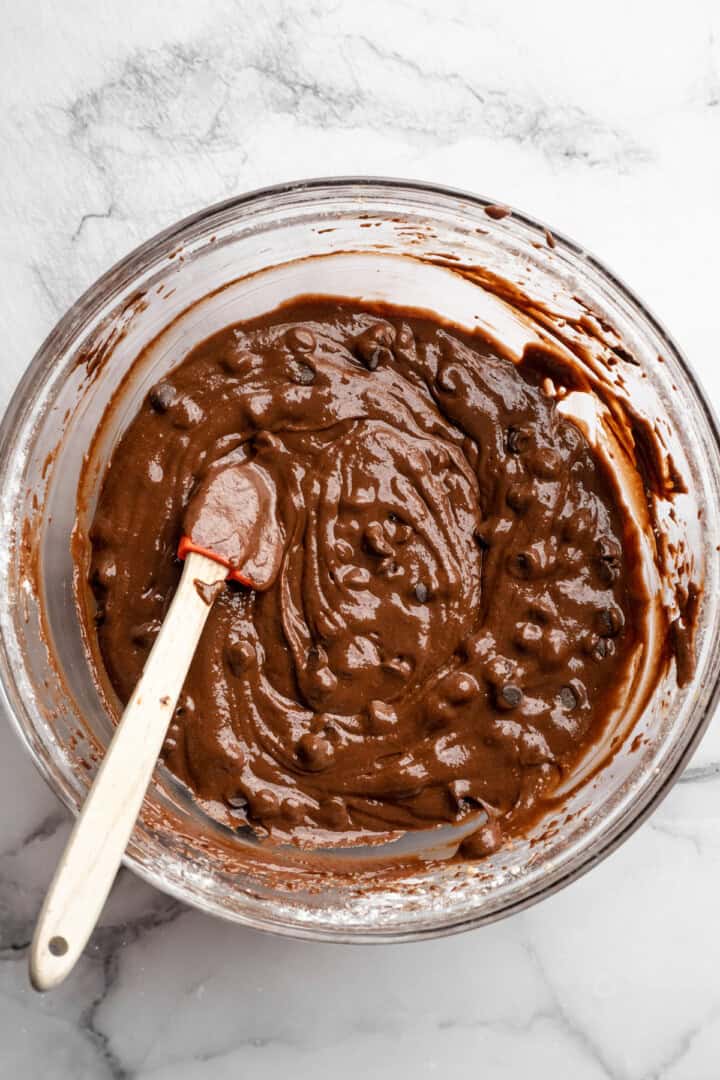 Brownie batter in glass bowl with rubber spatula.