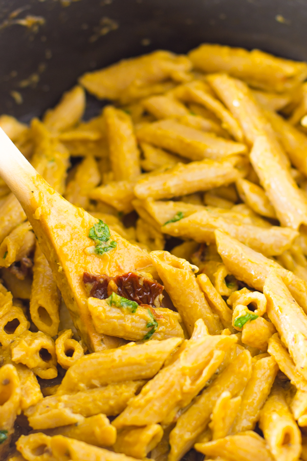 Alfredo penne pasta stirred with with sun dried tomatoes in a  black pot.