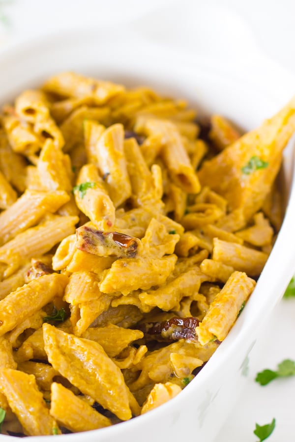 Close up of alfredo penne pasta with sun dried tomatoes in a white dish.