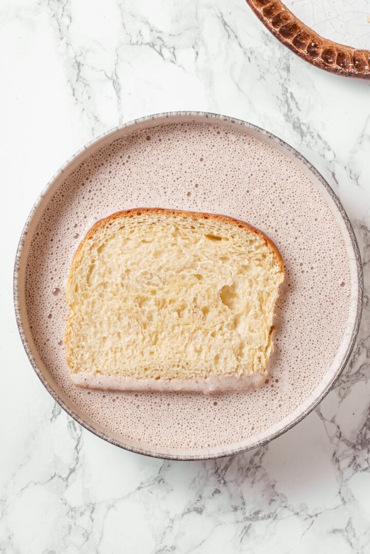Slice of bread in bowl of custard.