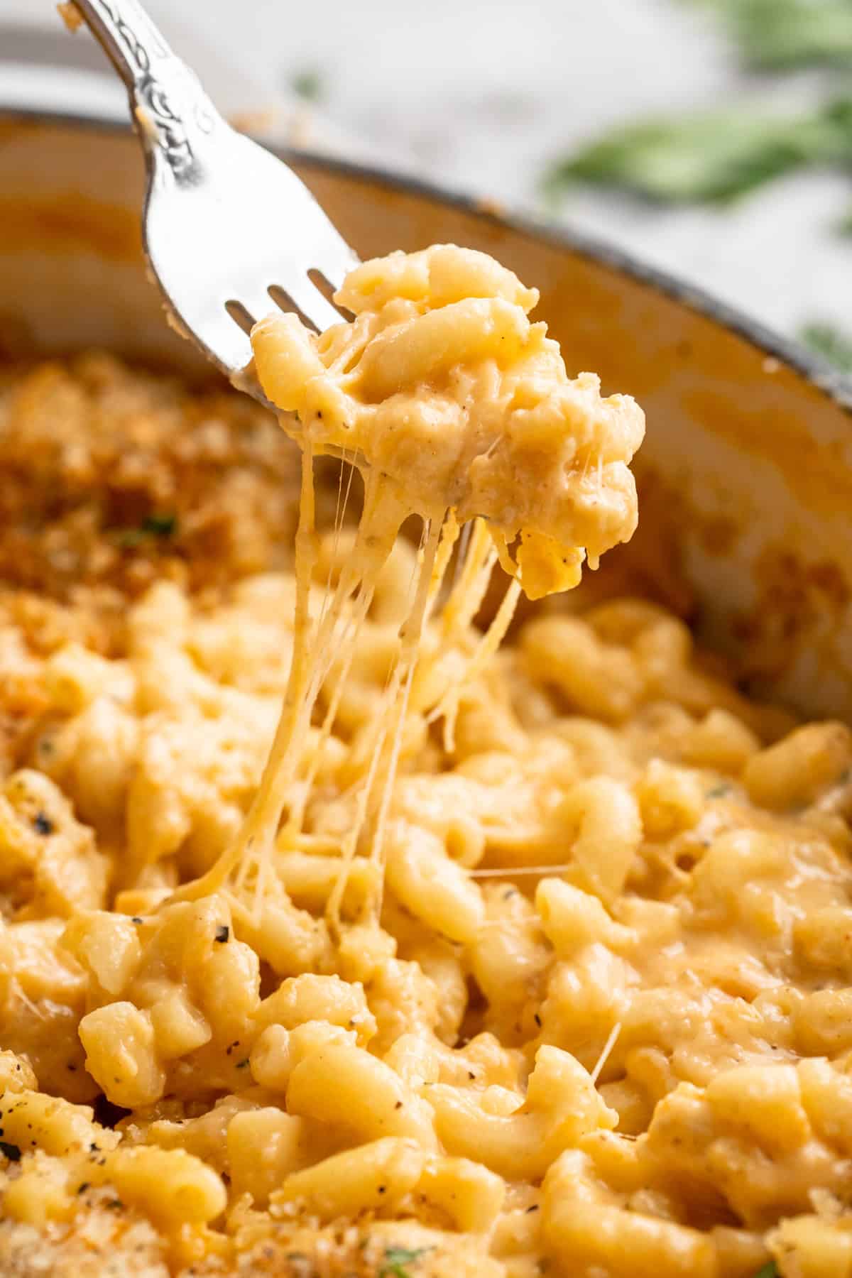 Forkful of vegan mac and cheese being lifted from skillet, showing cheese pull.