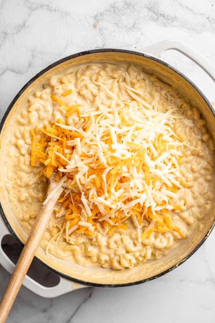 Stirring shredded vegan cheese into skillet of mac and cheese.