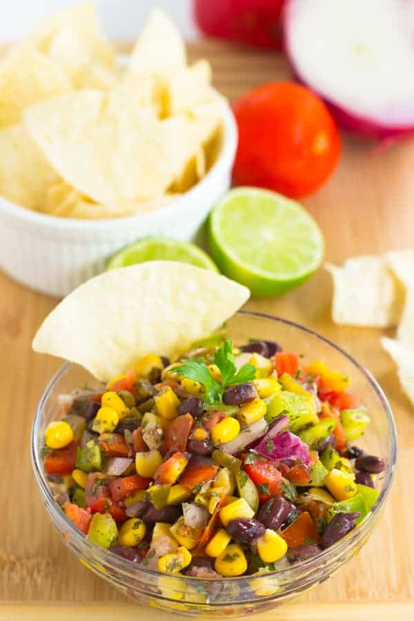 A glass bowl full of black bean salsa with a chip dipped in and lime in the background. 