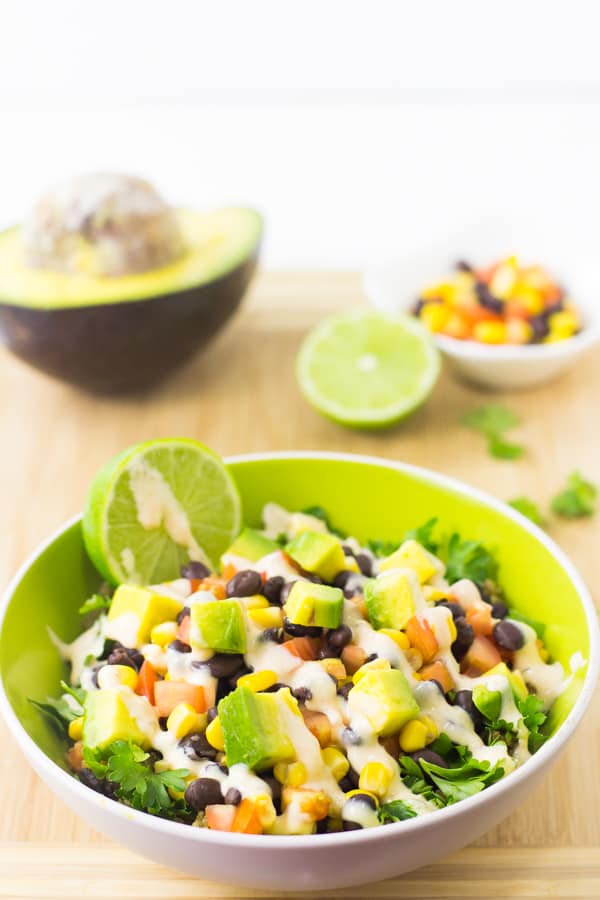 Quinoa and black bean burrito bowl on a wood table top with wedges of lime. 