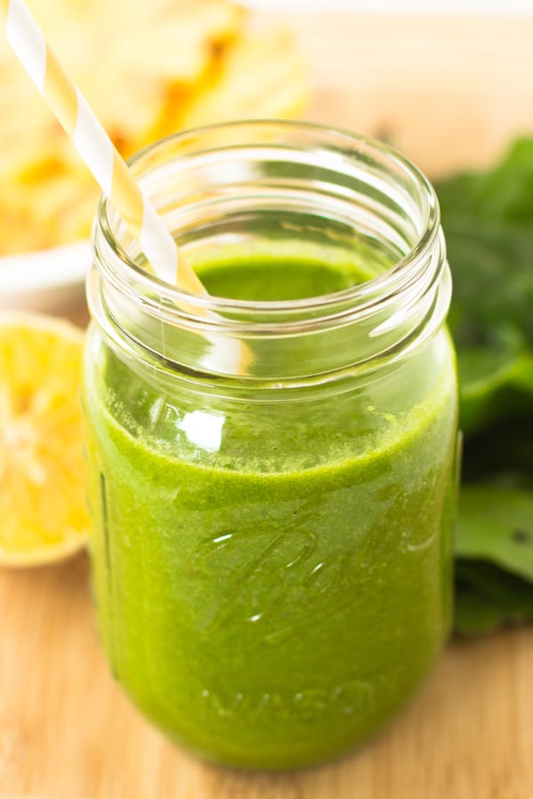 A tropical green smoothie in a glass mason jar with a yellow straw. 