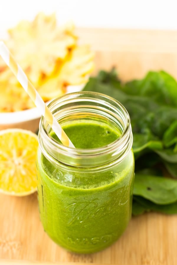 A tropical green smoothie in a mason jar with a yellow straw.