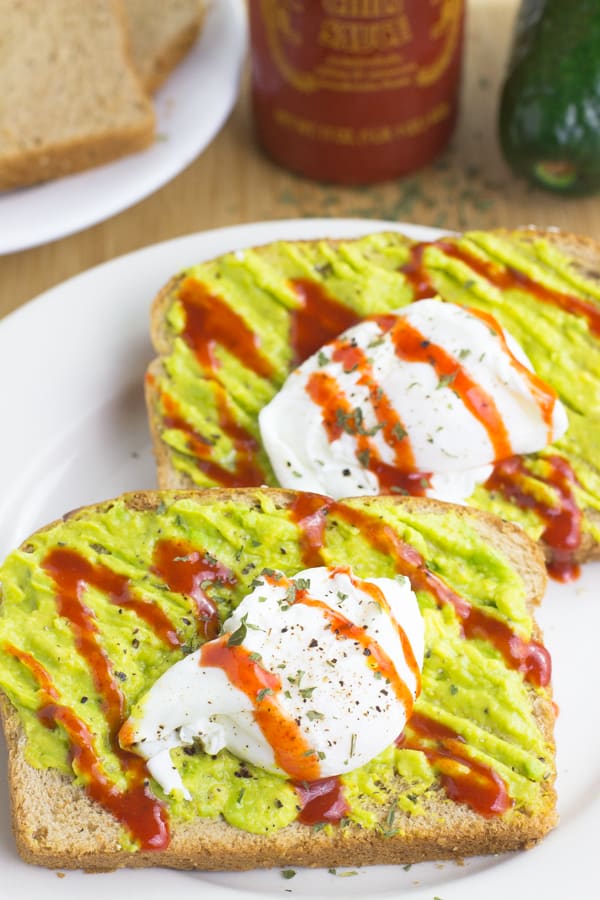 Two sriracha poached eggs and avocado smash toast on a white plate.