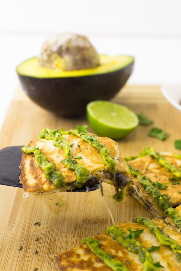 A spatula holding a slice of mexican quesadillas with avocado cilantro cream sauce.