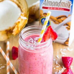 Strawberry coconut smoothie in a mason jar wit a straw and strawberries.