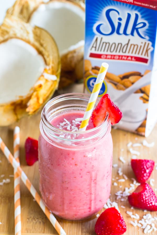 A strawberry coconut smoothie on a mason jar with a yellow straw. 