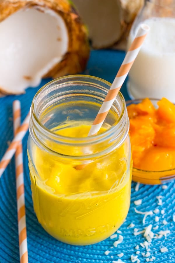 Close up of mango coconut smoothie in a mason jar with a yellow straw.