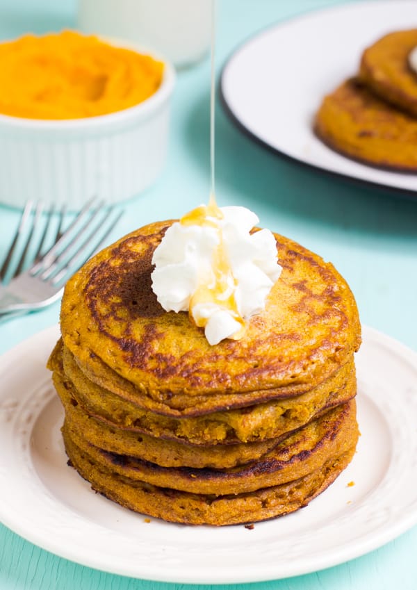 A stack of gluten free pumpkin pancakes with whipped cream on top. 