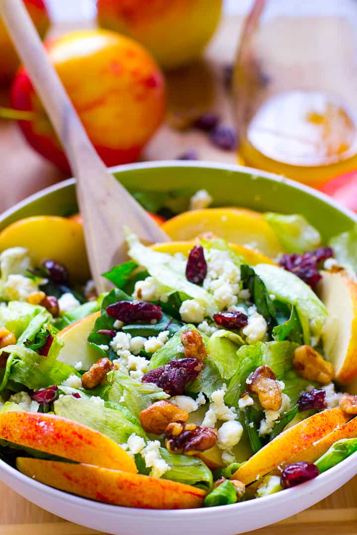 A green bowl with apple, candied walnuts and blue cheese salad and a spoon tossing it. 