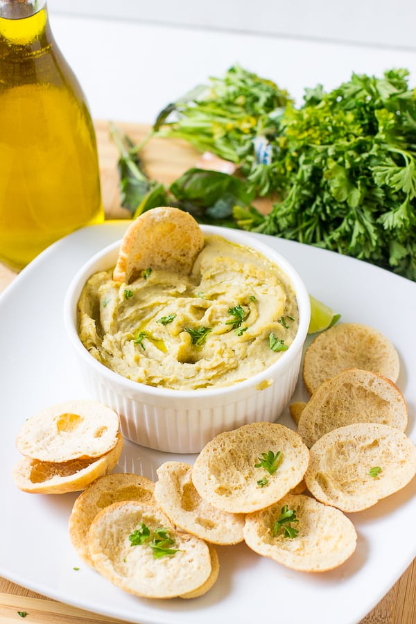 Herbed roasted garlic white bean dip in a white ramekin with chips around it. 