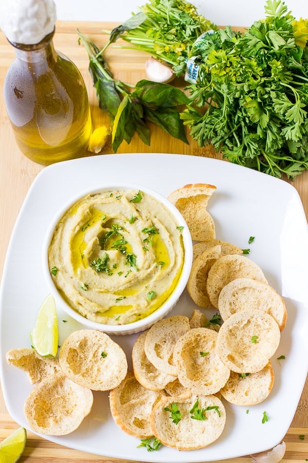 Top down shot of herbed roasted garlic white bean dip in a white ramekin with chips on the side. 