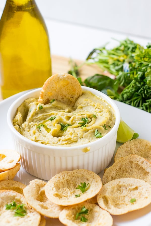 Herbed roasted garlic white bean dip in a ramekin with chips on the side. 