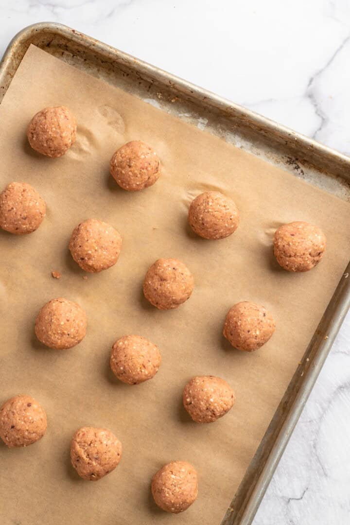 Overview of unbaked chickpea and beet vegetarian meatballs on parchment-lined sheet pan