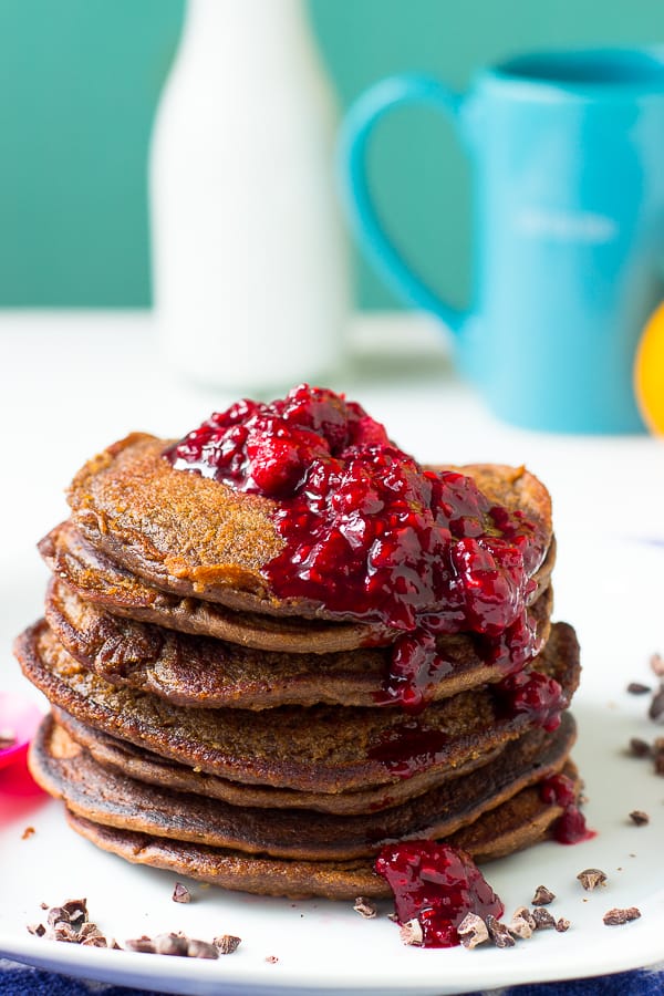 Chocolate peanut butter pancakes covered in raspberry compote on a white plate.