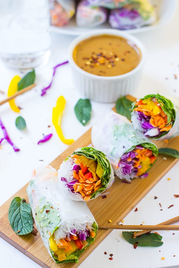 Four spring rolls on wood board with peanut ginger sauce in background