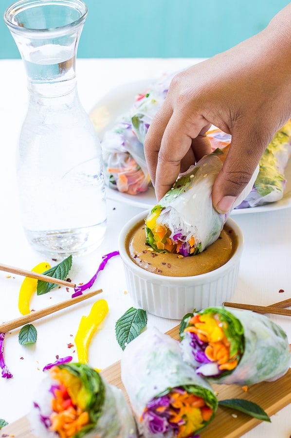 A hand dipping a summer roll into bowl of peanut sauce