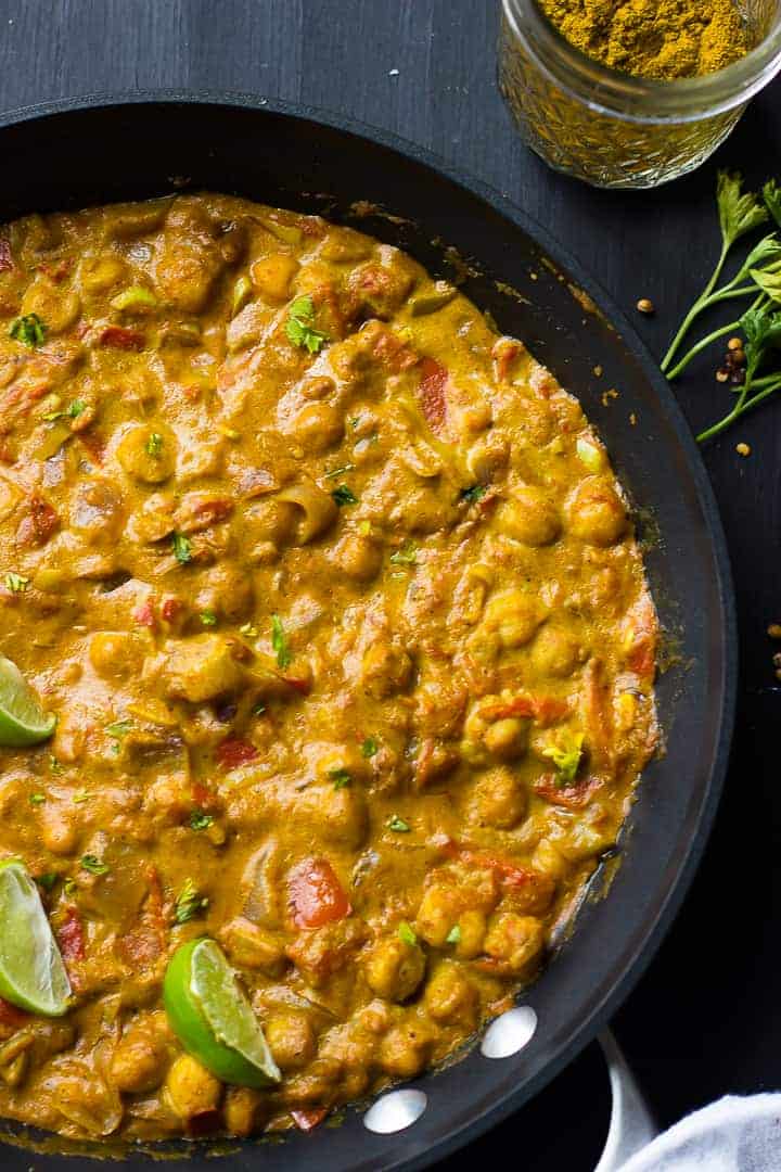 Overhead shot of creamy vegan coconut chickpea curry with lime wedges in a black skillet.