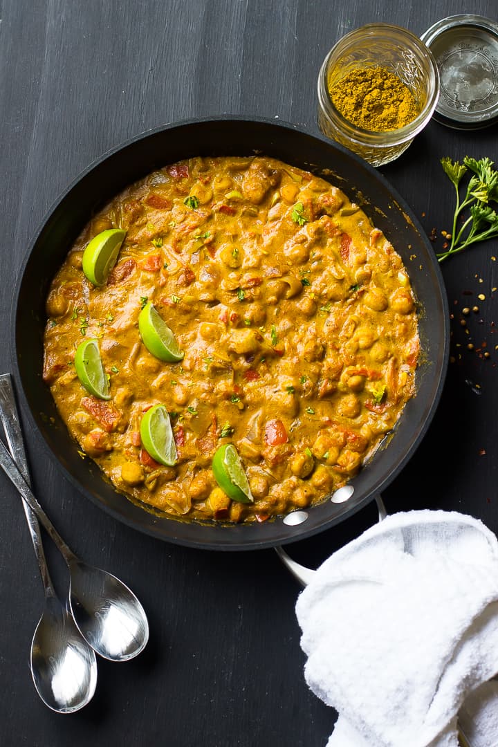 Overhead shot of chickpea curry in a black skillet with lime wedges. 