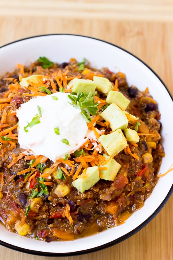Quinoa chili in a bowl topped with diced avocado, cheese and sour cream. 